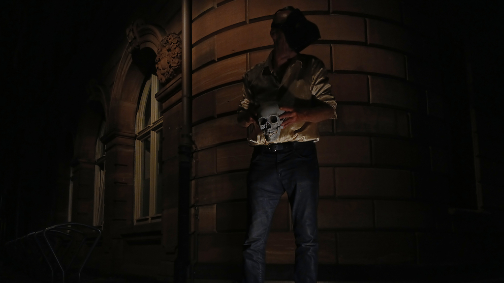 Mann mit Vogelmaske hält Totenschädel in der Hand